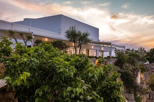 Un edificio moderno con techo plano, rodeado de abundante vegetación y un paisaje rocoso.