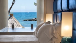 A bedroom with a view of the sea, a bed, a nightstand, and a lamp.