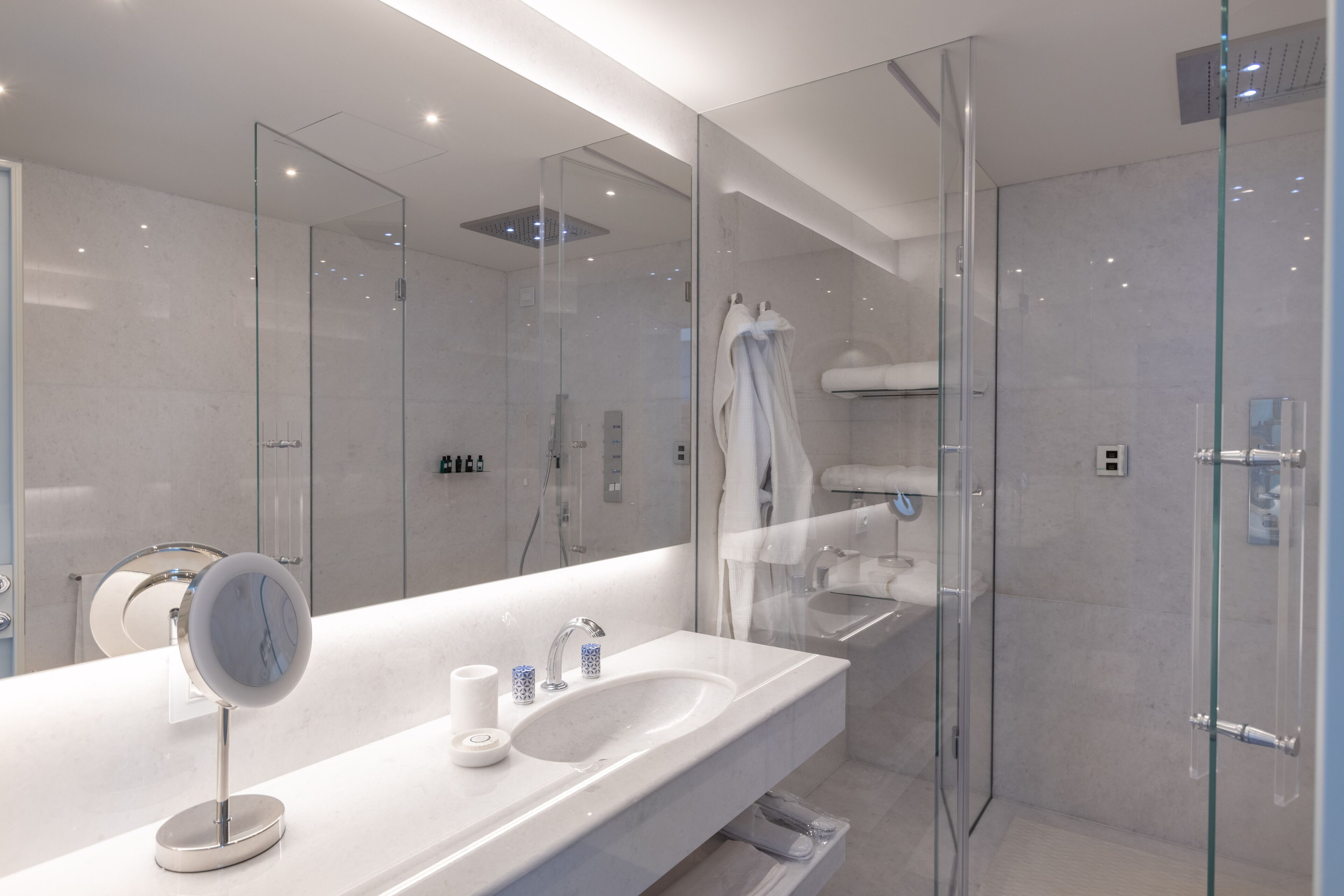 Een moderne badkamer met een glazen douchecabine, een grote spiegel en een witte wastafel.