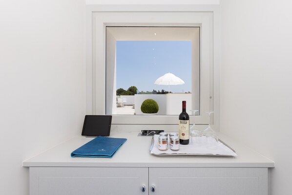 A bathroom with a window, a laptop, a bottle of wine, and toiletries on the counter. - Grotta Palazzese Beach Hotel (Polignano a Mare)