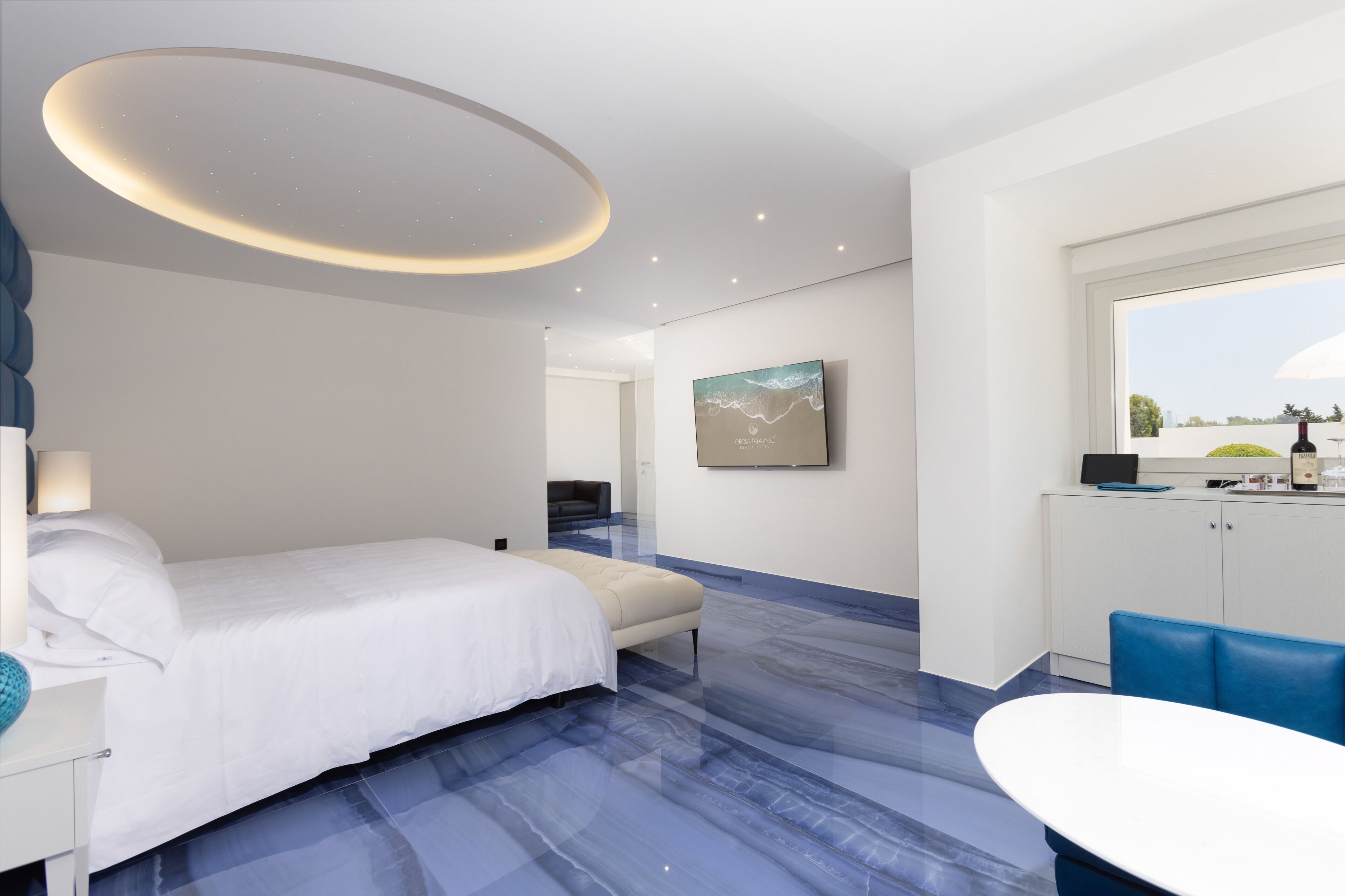 Een moderne hotelkamer met een bed, een bureau, een stoel, een eettafel, een raam en een schilderij aan de muur.
