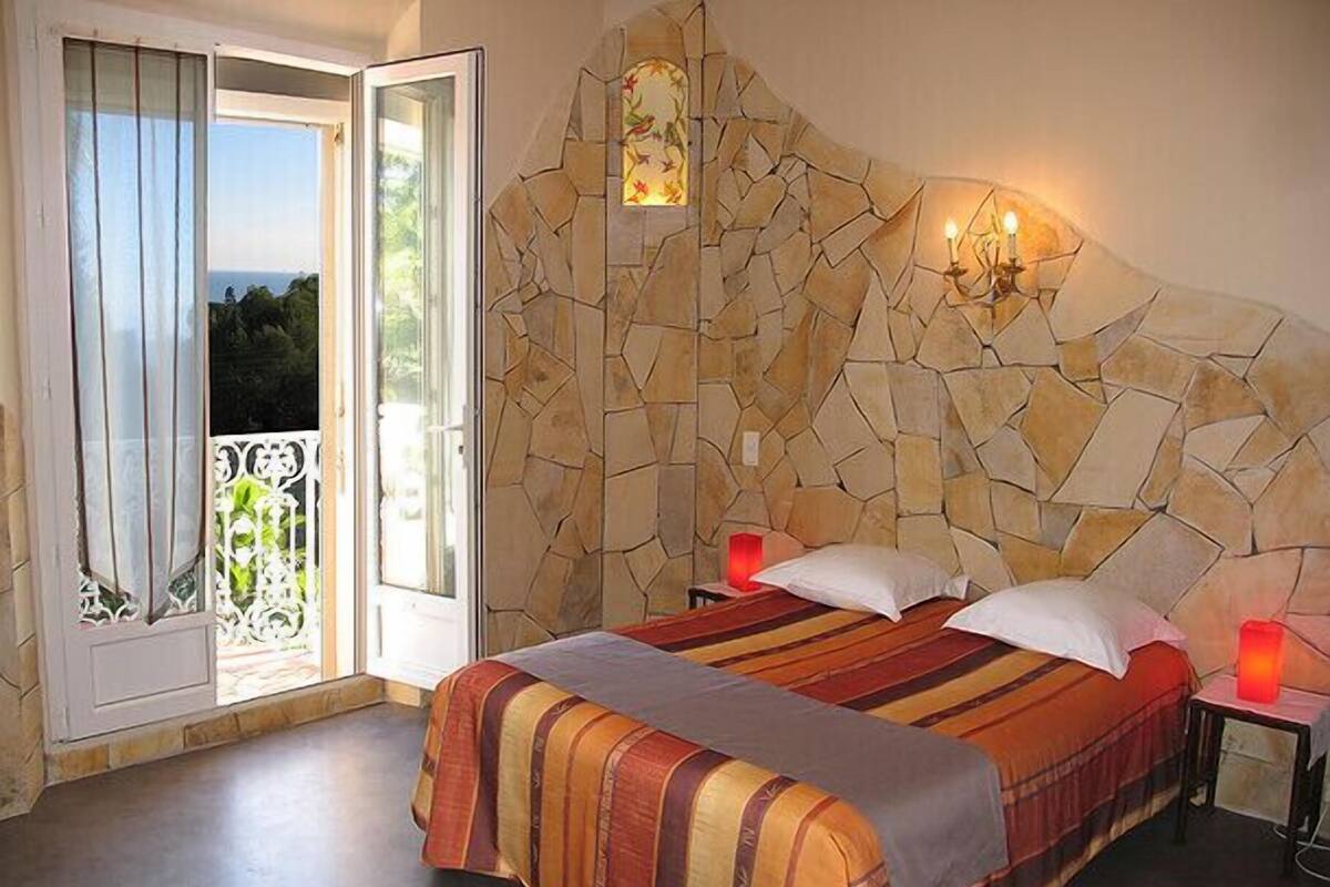 A bedroom with a stone wall, a bed with striped bedding, two bedside lamps, and a view through a sliding glass door.