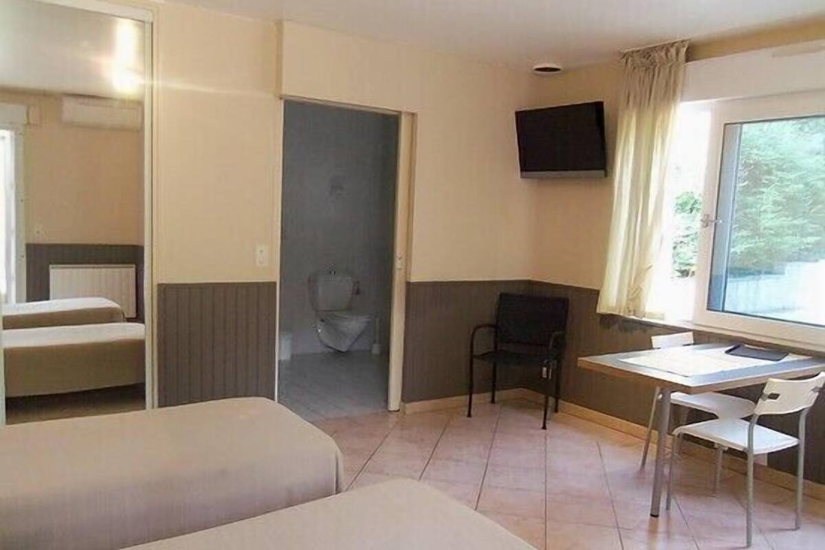 A room with two beds, a desk, a chair, a TV, and a window with curtains.