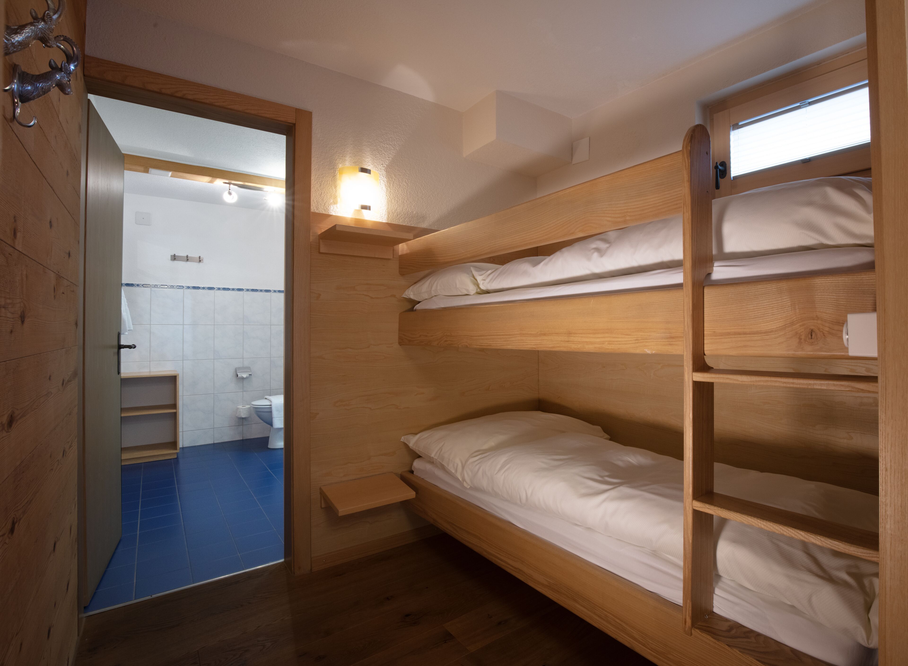 A compact, wooden bunk bed room with a small shelf and a light fixture above the bed.