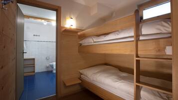 A compact, wooden bunk bed room with a small shelf and a light fixture above the bed.