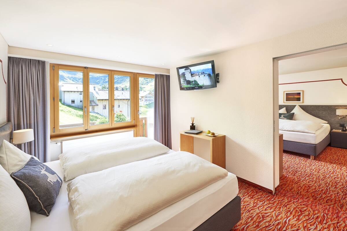 Ein Hotelzimmer mit zwei Betten, einem Fernseher, einem kleinen Tisch und Blick auf ein Bergdorf.
