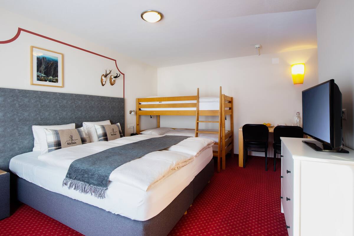 Ein Hotelzimmer mit einem Etagenbett, einem Schreibtisch mit Computer, einem Fernseher und einem roten Teppichboden.
