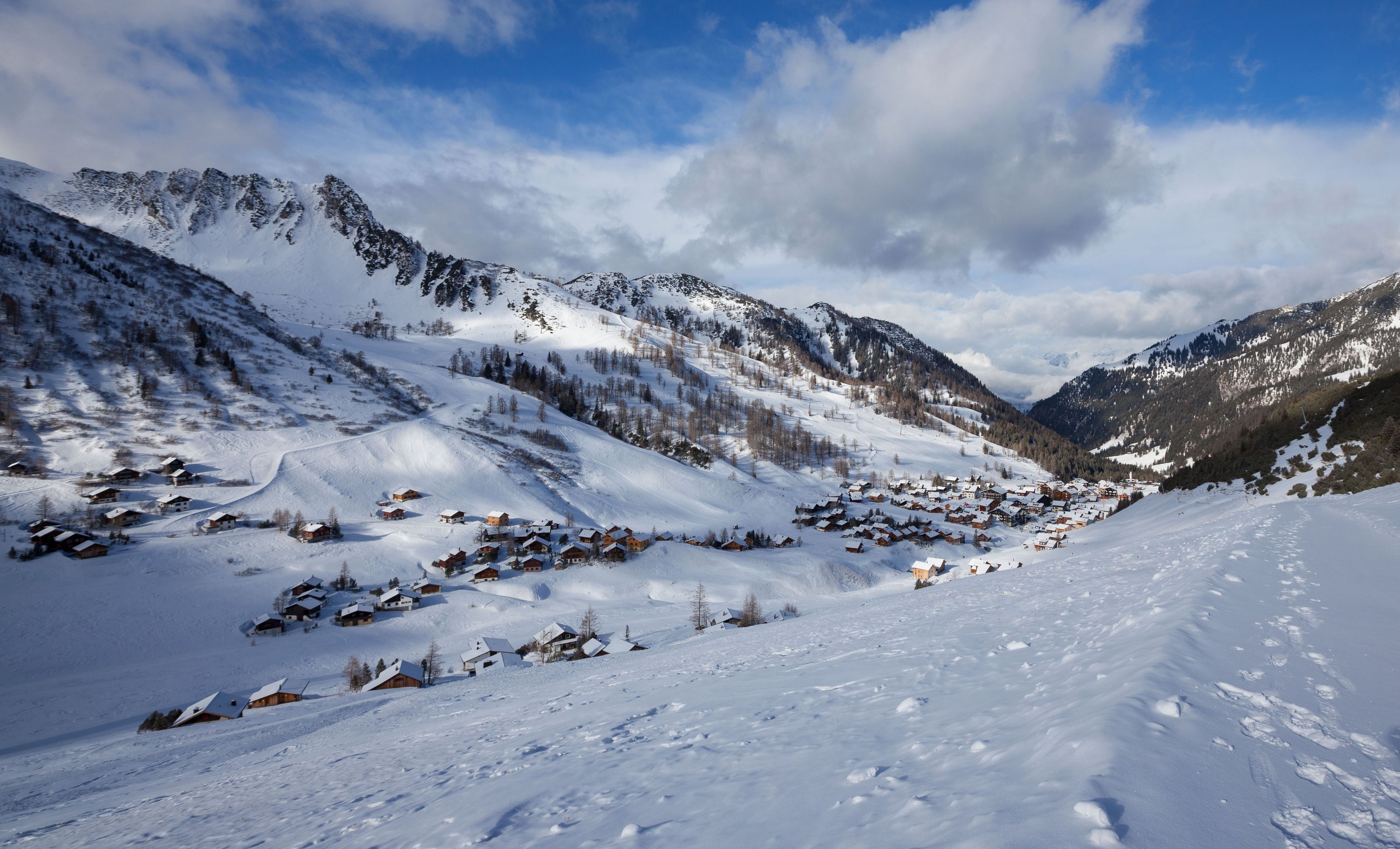 Un pueblo cubierto de nieve en la montaña con casas de madera tradicionales, cielo despejado y un valle entre las montañas.