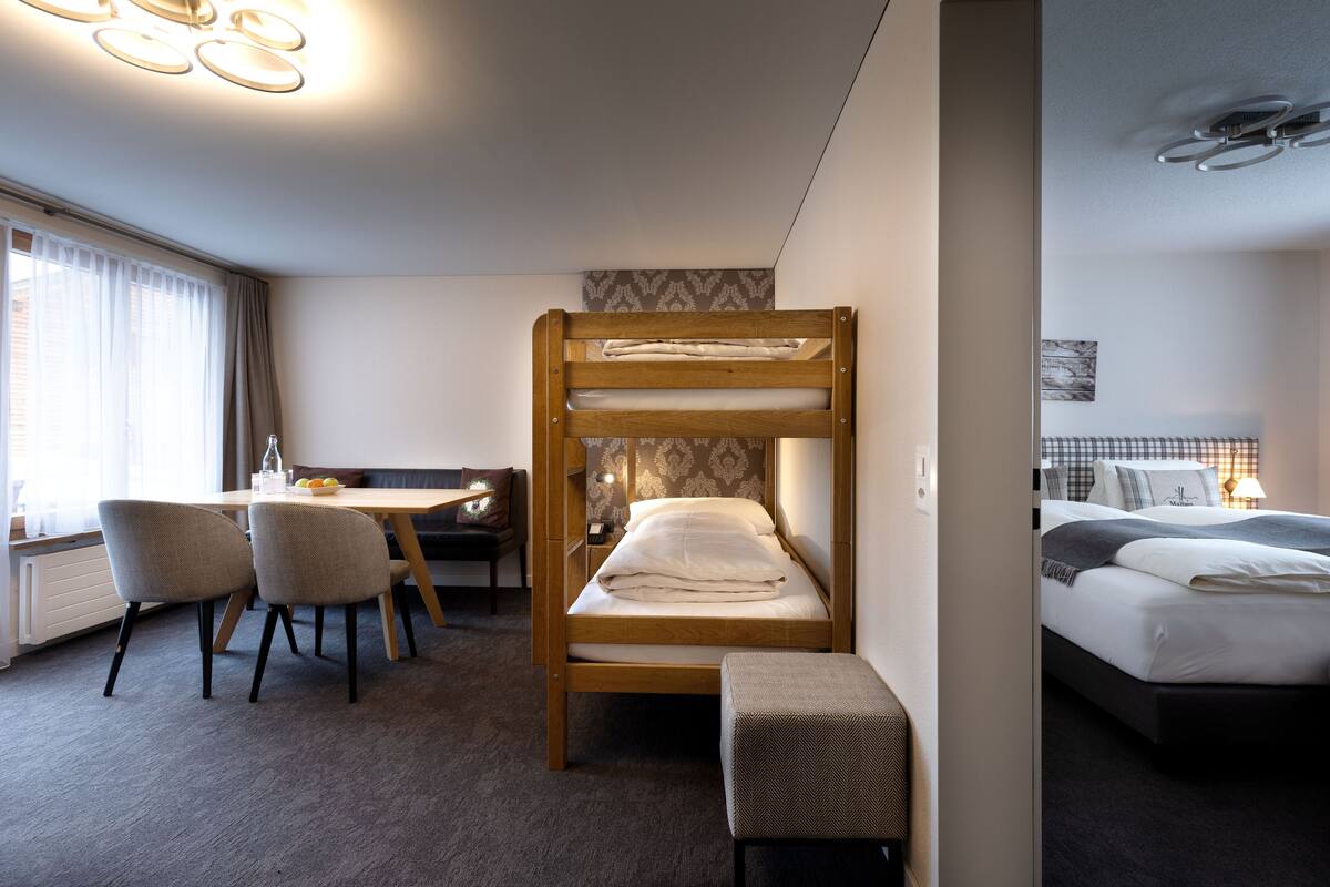 Ein Hotelzimmer mit einem Etagenbett, einem Schreibtisch mit Stühlen, einem kleinen Tisch und einer Bank.