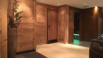 Un pasillo interior de madera con un jarrón grande de plantas secas, una puerta y un piso de baldosas.