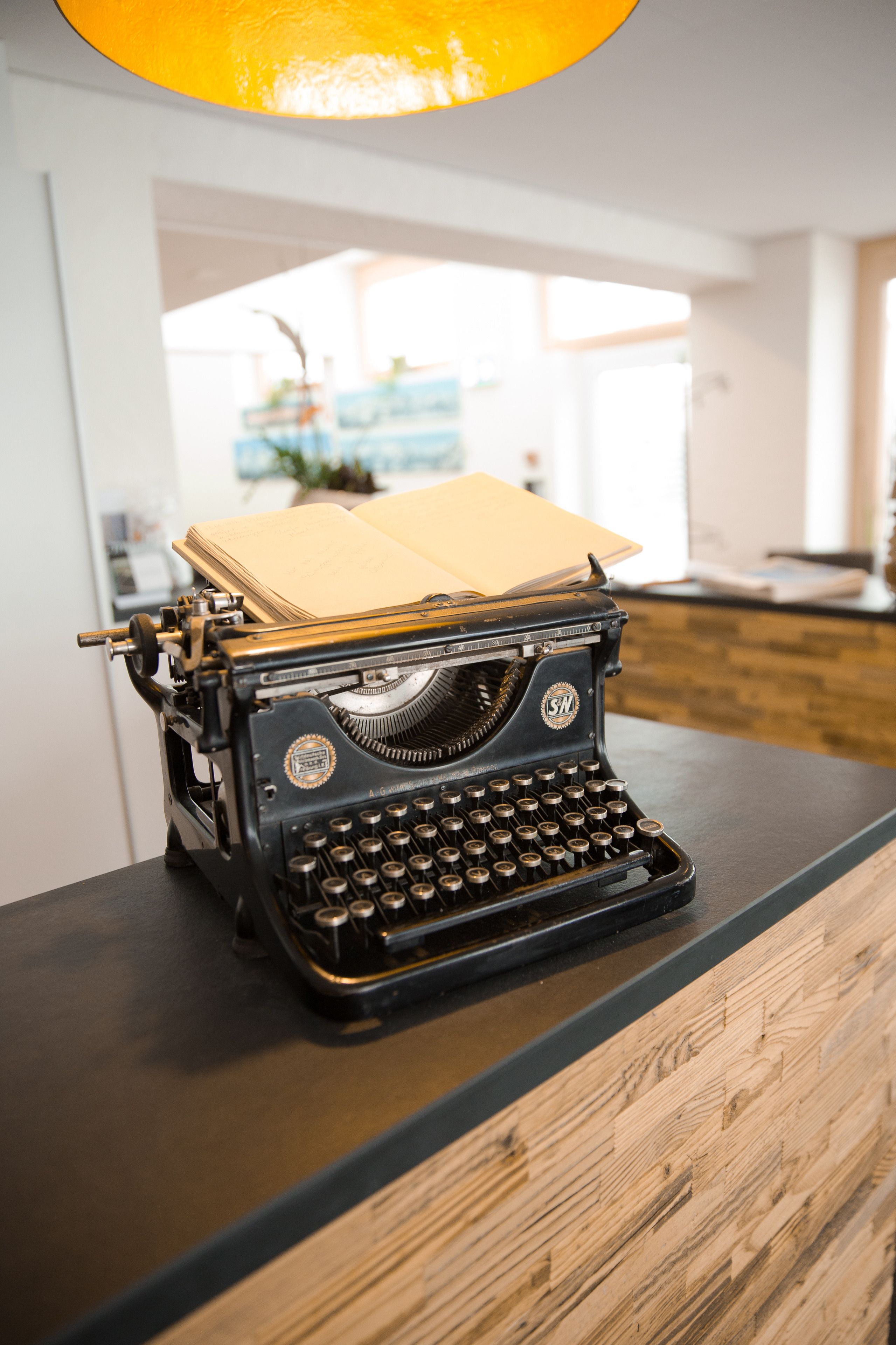 A vintage typewriter on a wooden desk in a room with a modern kitchen in the background.