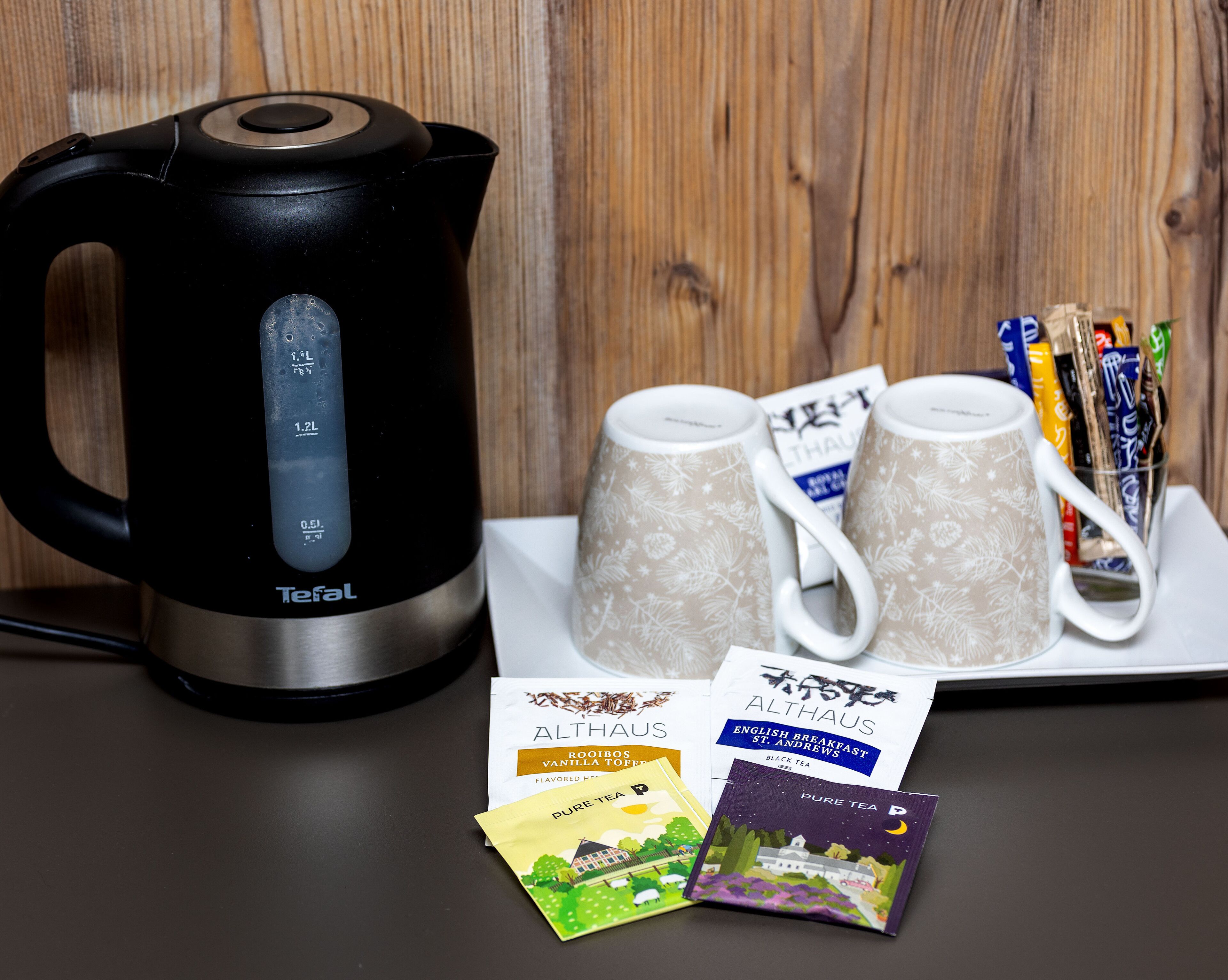 A black electric kettle, two patterned mugs, and tea bags on a table.