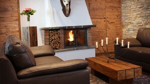 Ein gemütliches Wohnzimmer mit Ledersofas, einem Kamin mit Steinverkleidung und einem aufgehängten Hirschschädel.