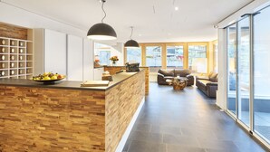 Eine moderne Küche mit einer Holzinsel, einer Sitzecke mit Sofas und großen Fenstern mit Blick ins Freie.
