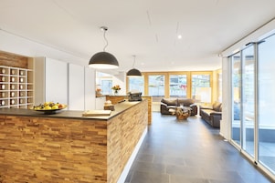 Una cocina moderna con una isla de madera, una zona de estar con sofás y ventanas amplias que ofrecen vistas al exterior.