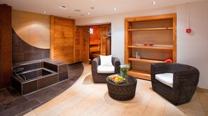 A spa area with a stone bathtub, wicker chairs, and a wooden shelf with a vase of flowers.