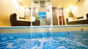 Ein Pool mit zentralem Wasserspiel, zwei Korbsessel mit Kissen und eine Wand mit einem gerahmten Bild.