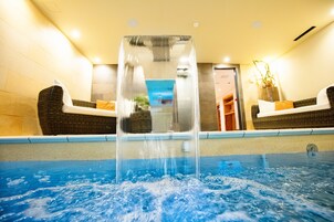 Una piscina con una fuente central, dos sofás de mimbre con cojines, y una pared con un cuadro enmarcado.