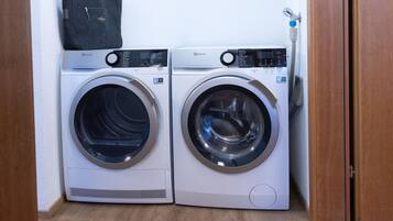 Two front-loading washing machines side by side in a laundry room with a wooden floor and a white wall.