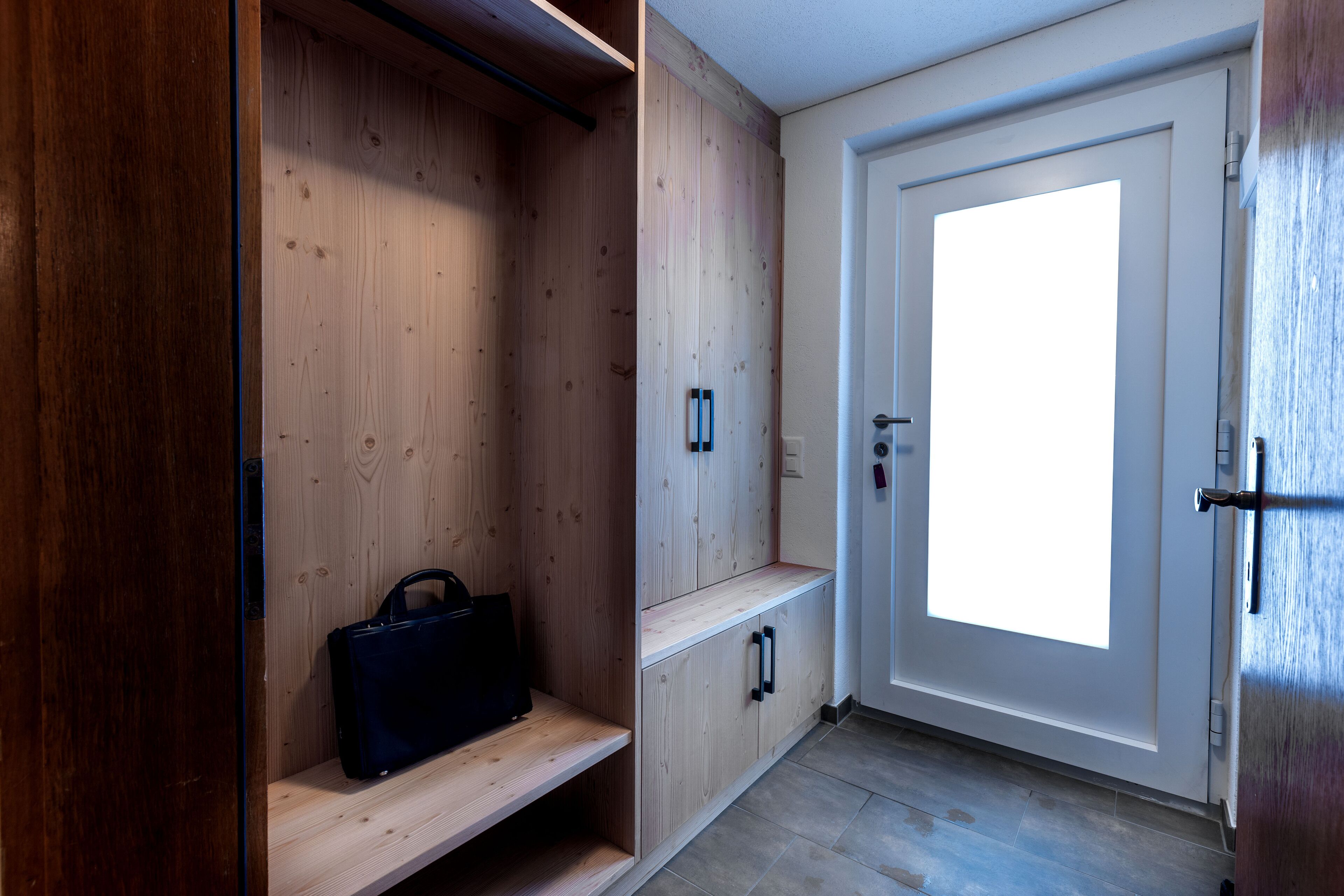 Un couloir avec des casiers en bois, un banc et une porte dotée d’une grande fenêtre.