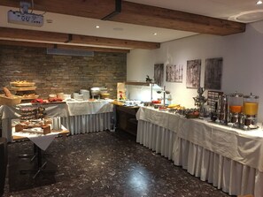 Ein Frühstücksbuffet mit verschiedenen Speisen und Getränken, eine Steinwand und Holzbalken an der Decke.