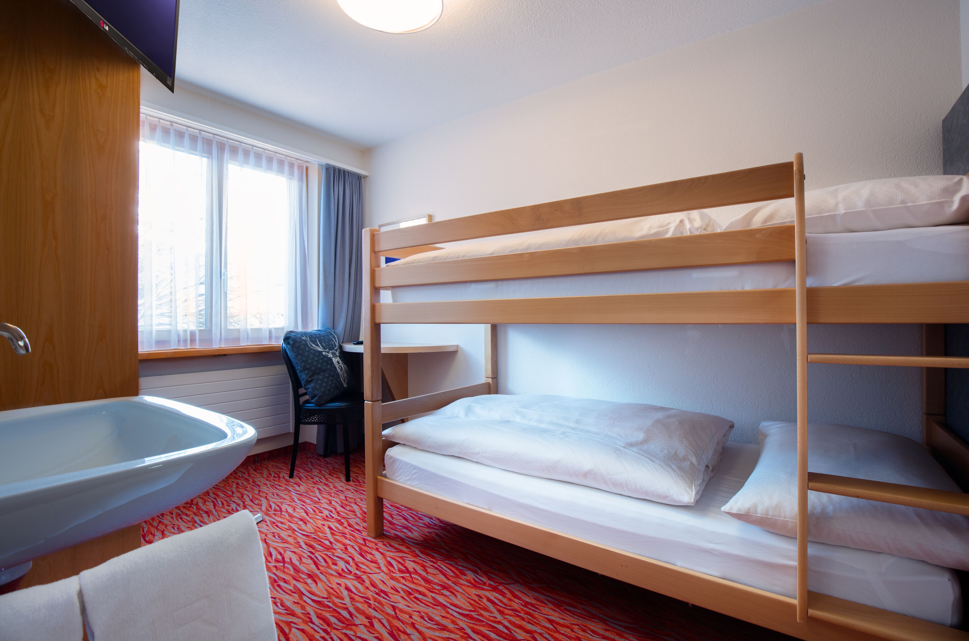 Dormitorio con literas, un lavabo, una silla y una ventana con cortinas.