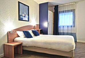 A neatly arranged hotel room with a large bed, bedside tables, a framed picture on the wall, and a window with curtains. - Art Hotel Paris Est (Pantin)