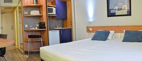A hotel room with a bed, a desk, a chair, a mini-fridge, and a microwave.