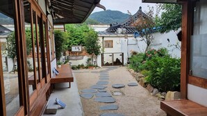 A traditional courtyard with stone pathways, wooden benches, and lush greenery. - Jeonju Greem (Jeonju)