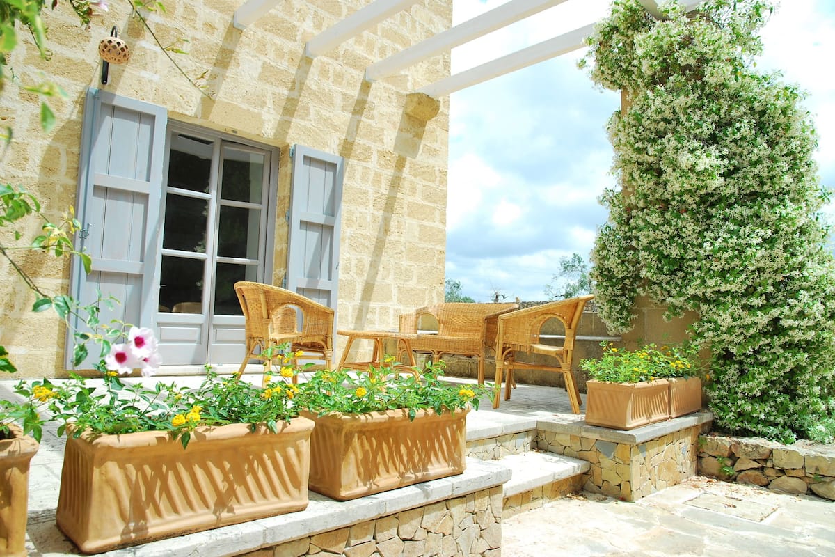 Un bâtiment en pierre doté d’un balcon, de meubles en osier et de plantes en pot.