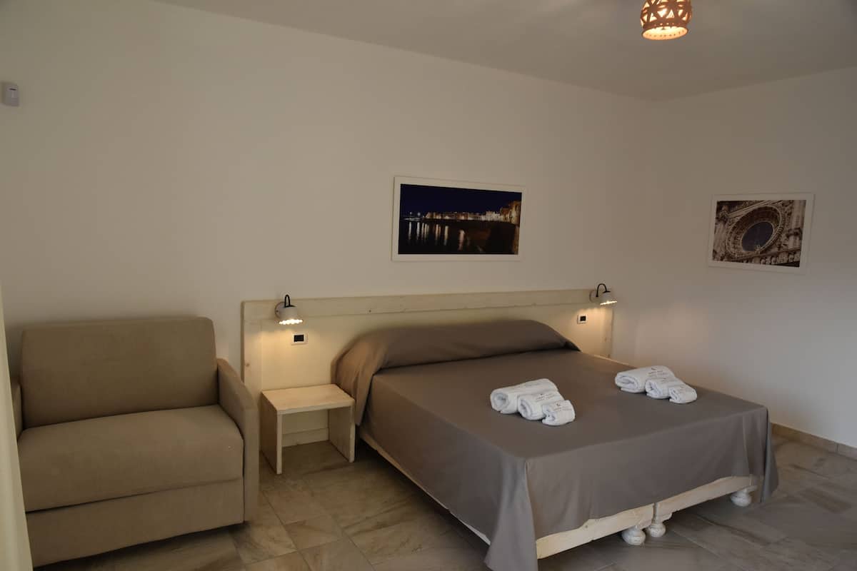 Une chambre à coucher comprenant un lit, un banc, un canapé et deux lampes fixées au mur.