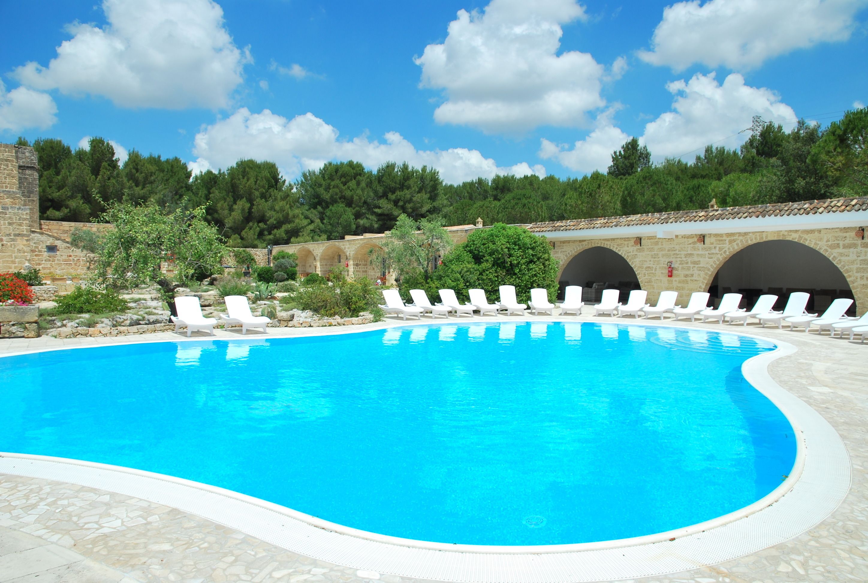 Una piscina con sillas de descanso blancas y un muro de piedra al fondo.