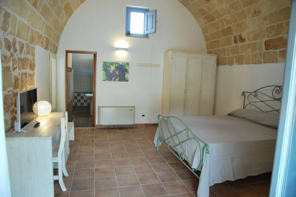 Une chambre à coucher avec un lit, un bureau avec une lampe, une armoire et une petite fenêtre.