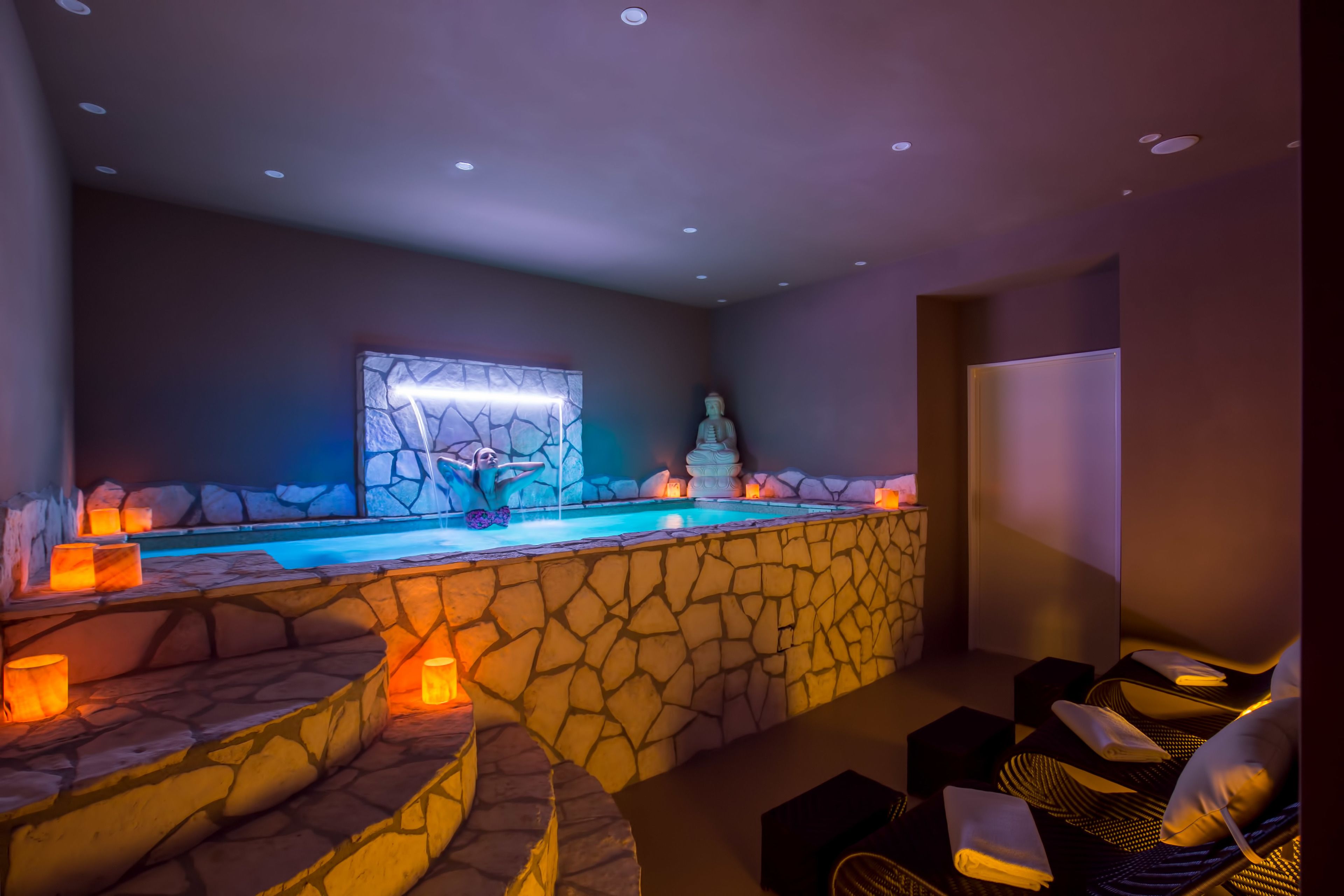 A spa area with a stone wall, a Buddha statue, and a pool.