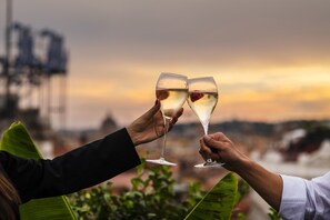 Zwei Personen stoßen mit Champagnergläsern inmitten einer Sonnenuntergangslandschaft an.