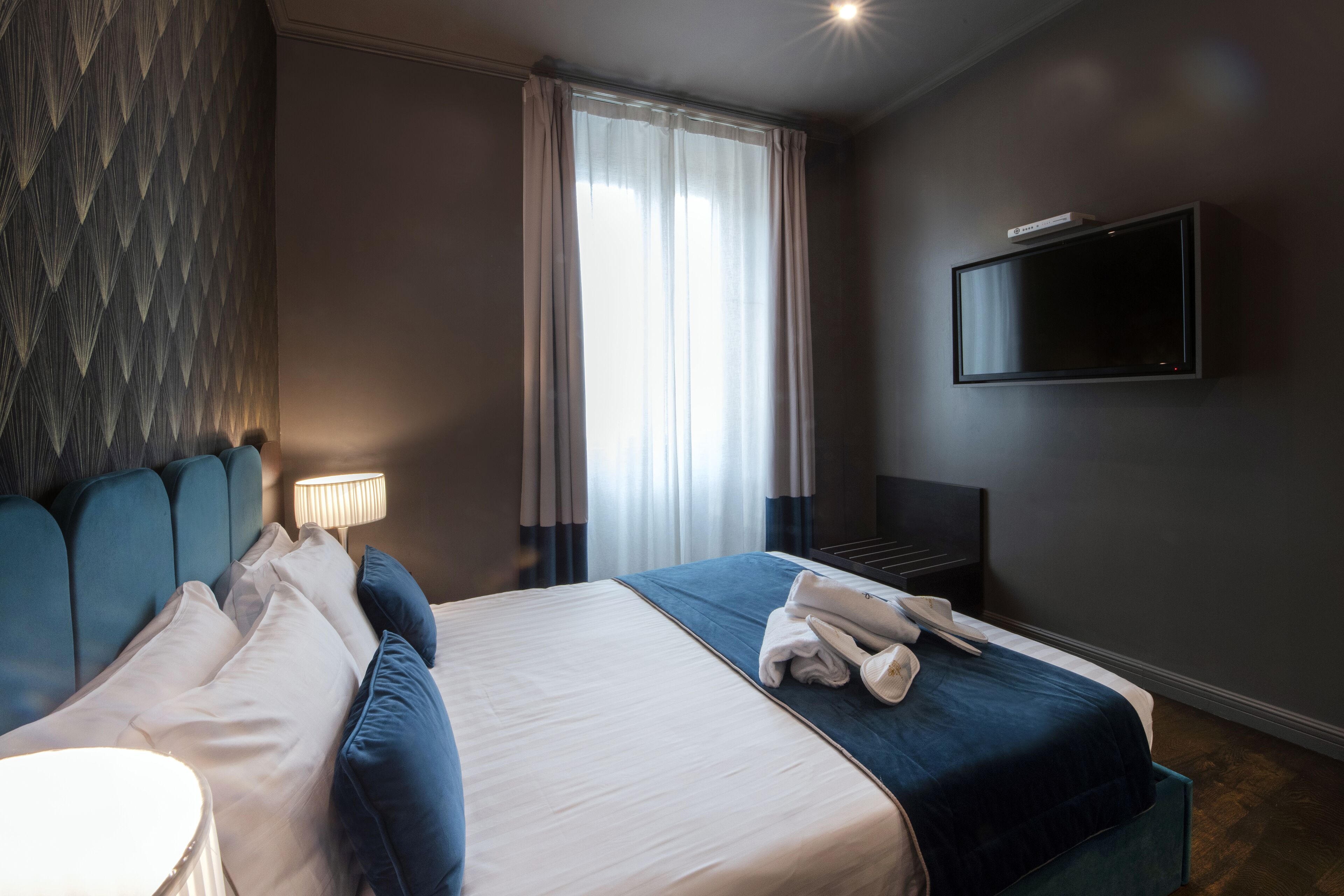 Una camera d'albergo con un letto grande, una televisione a parete e una finestra con tende.