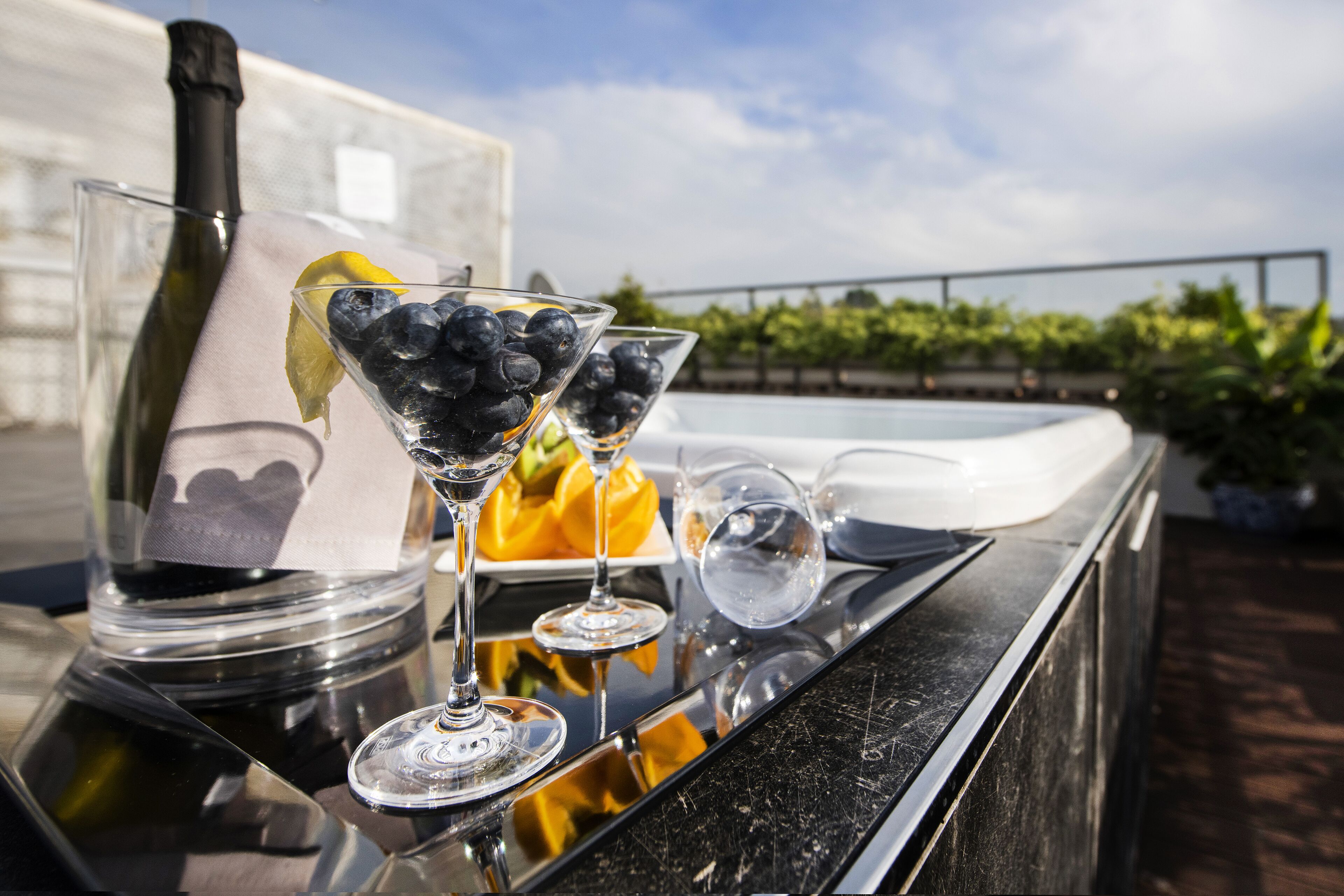 A bar area with a bottle of champagne, two glasses with blueberries, and a lemon slice.