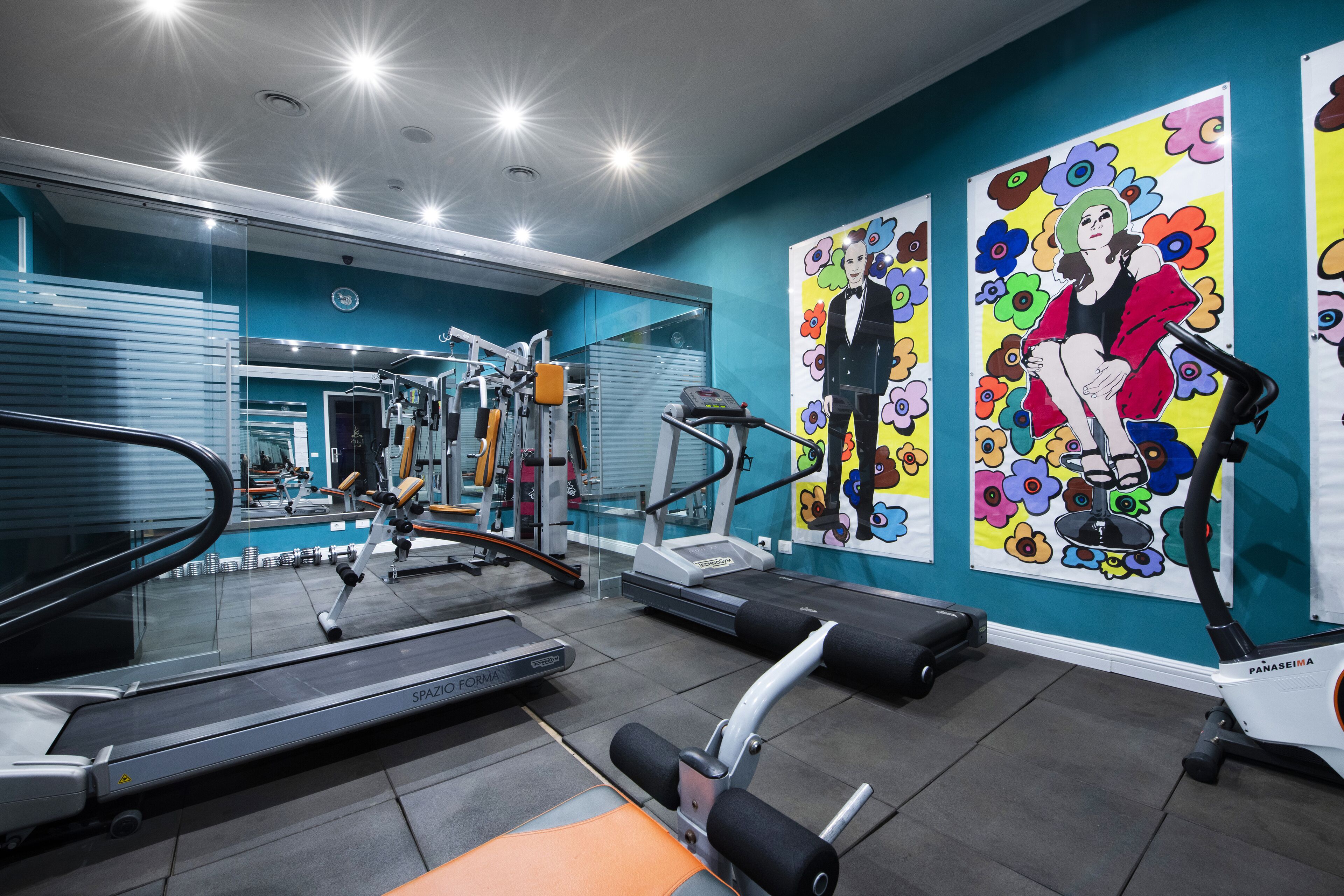 Una palestra con macchinari cardio, attrezzature per l'allenamento con i pesi e uno specchio a parete.