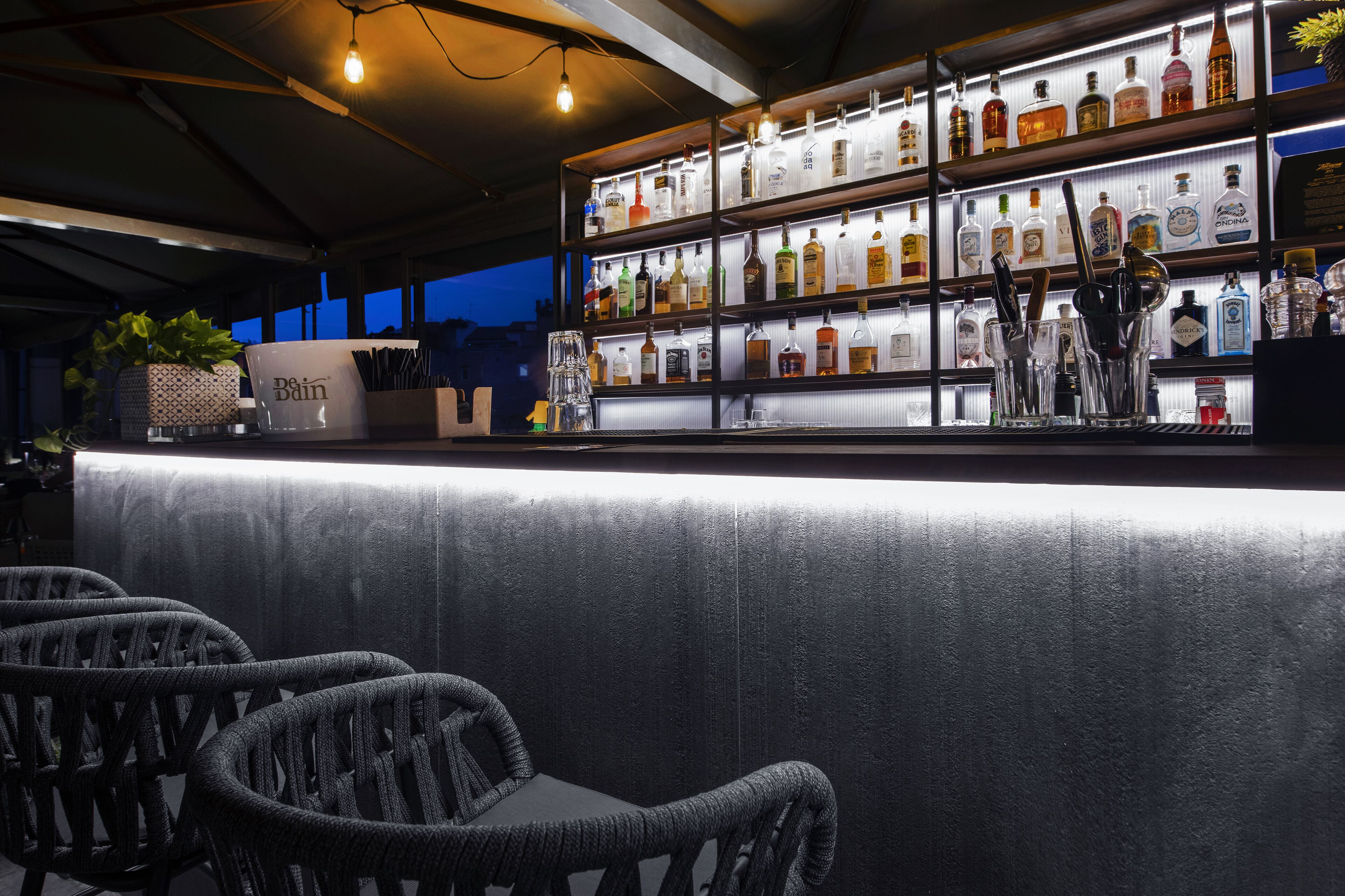 A bar area with wicker chairs, a counter with bottles, and a potted plant.