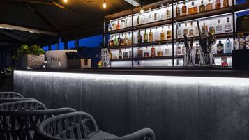 A bar area with wicker chairs, a counter with bottles, and a potted plant.