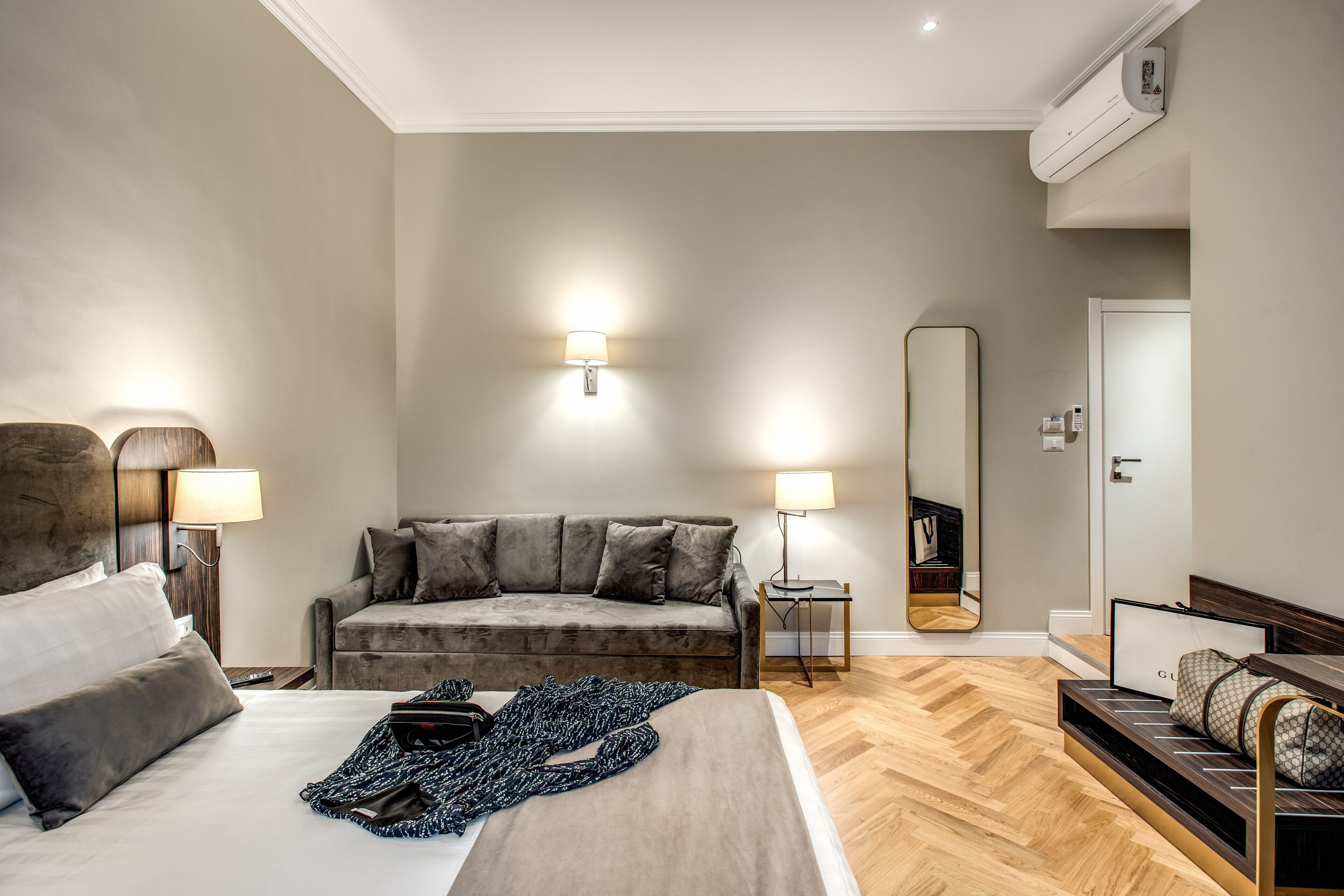 A modern hotel room with a large bed, a sofa, a small table, and a mirror.