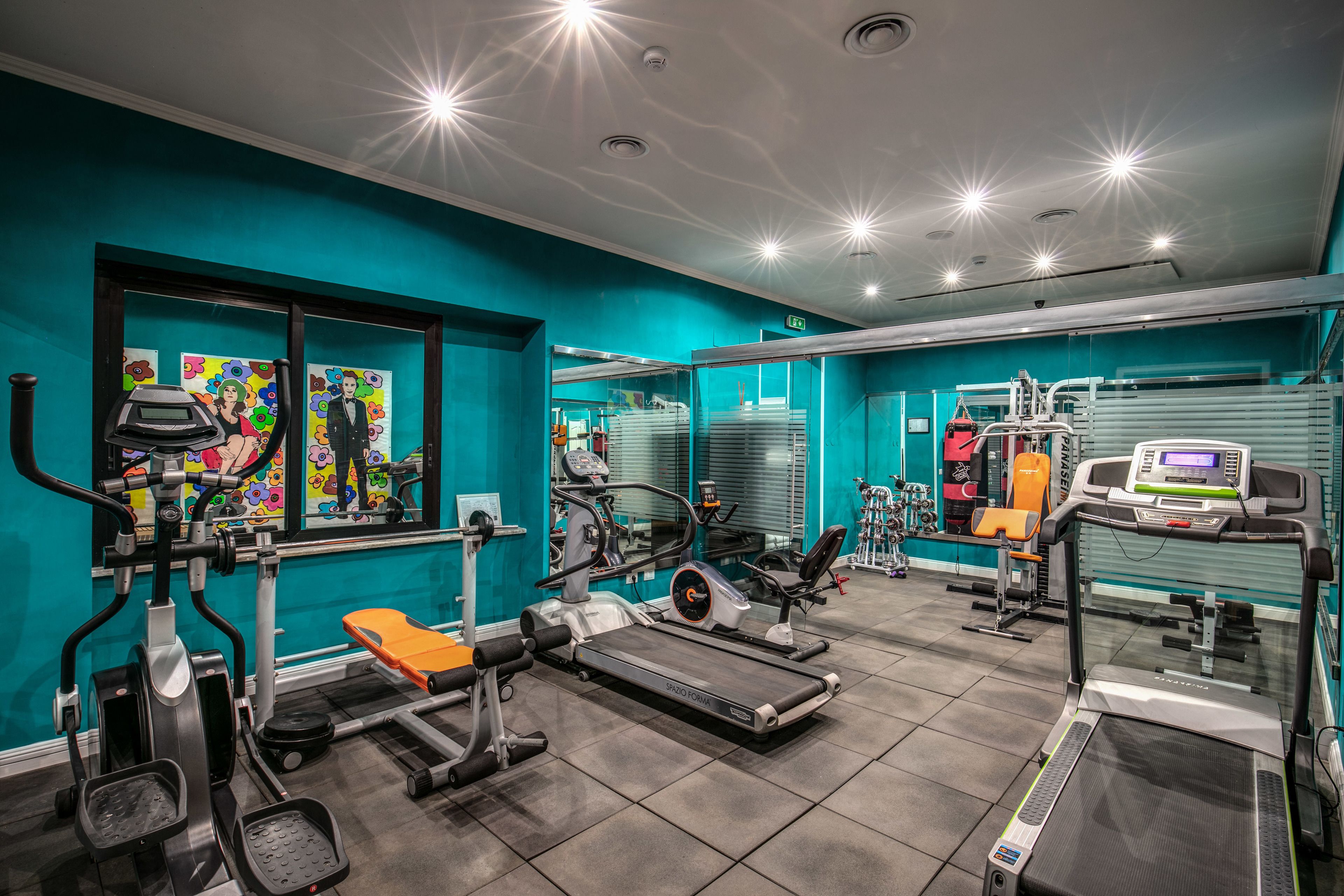 A gym with various exercise equipment, teal walls, and a large mirror.