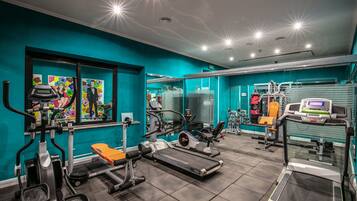A gym with various exercise equipment, teal walls, and a large mirror.
