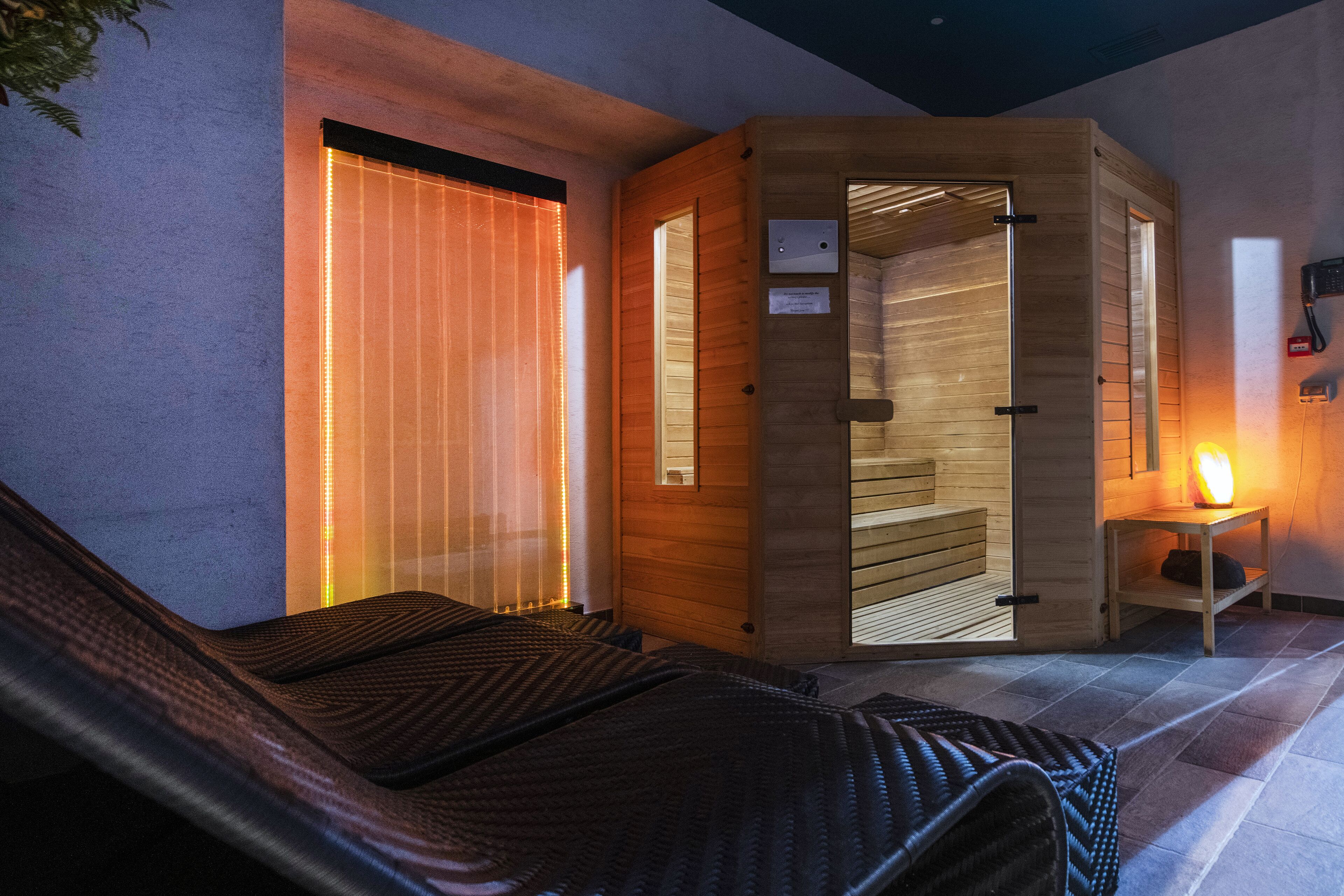 Una sauna con porta in legno, una panca e un piccolo tavolo con una luce.