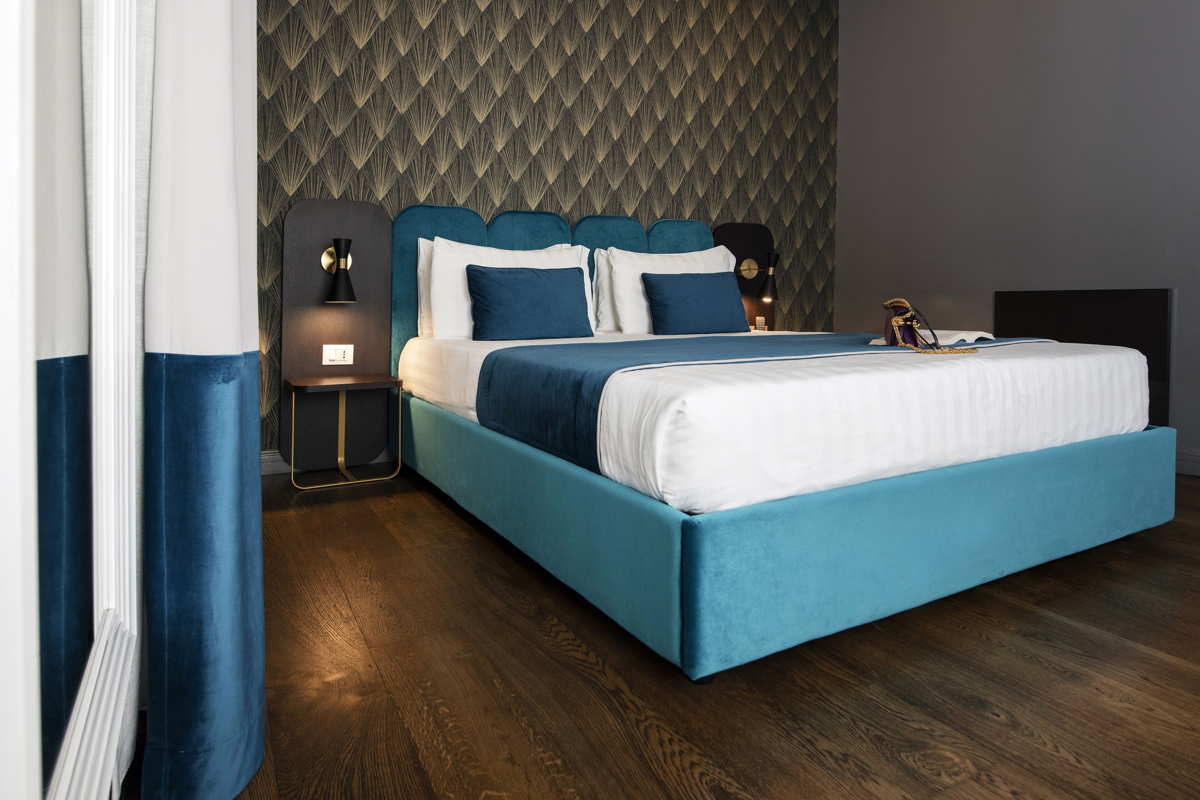 Un dormitorio moderno con una cama color turquesa, ropa de cama blanca y un papel tapiz estampado.
