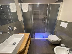 Une salle de bain moderne avec une douche à parois de verre, un meuble-lavabo en bois, un lavabo blanc et des toilettes.