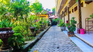 A narrow cobblestone pathway flanked by potted plants and a building with a tiled roof. - Bali Manik Beach Inn (Kuta)