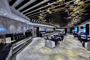 A modern hotel lobby with a long reception desk, multiple seating areas, and a unique ceiling design.