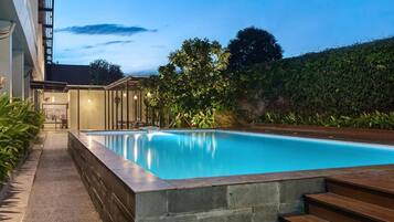 Une piscine bordée de pierres, entourée d’une allée pavée et d’une terrasse en bois.