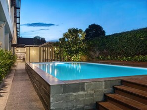 A swimming pool with a stone edge, surrounded by a paved walkway and a wooden deck. - Swiss-belinn Cibitung (Cikarang)